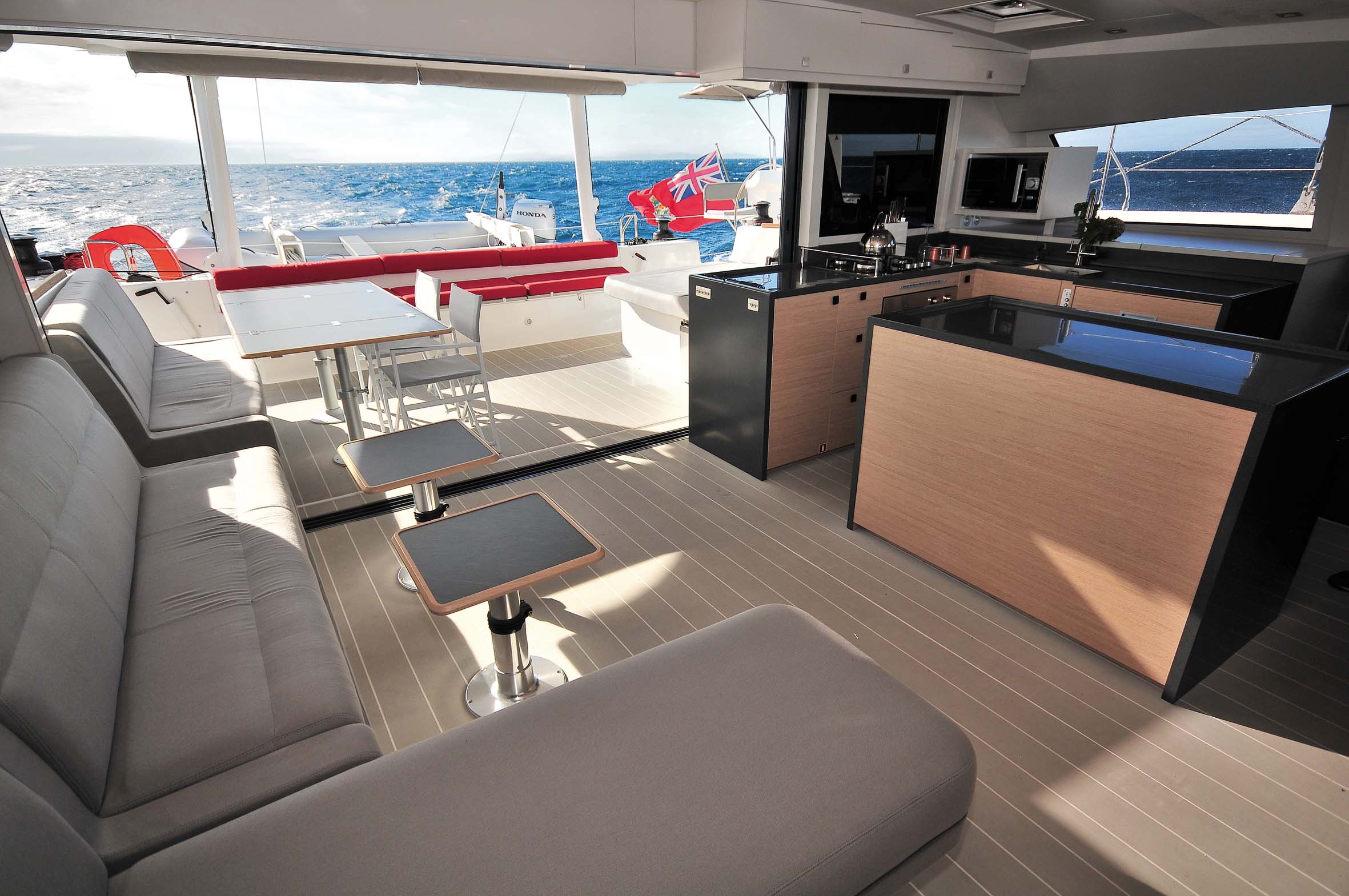 Le salon de pont est complètement ouvert sur l'extérieur grâce à la baie vitrée coulissante 3 panneaux, mais la table de cockpit peut rapidement prendre place à l'intérieur pour recréer une belle ambiance conviviale autour de la superbe cuisine et de l'îlot bar central.