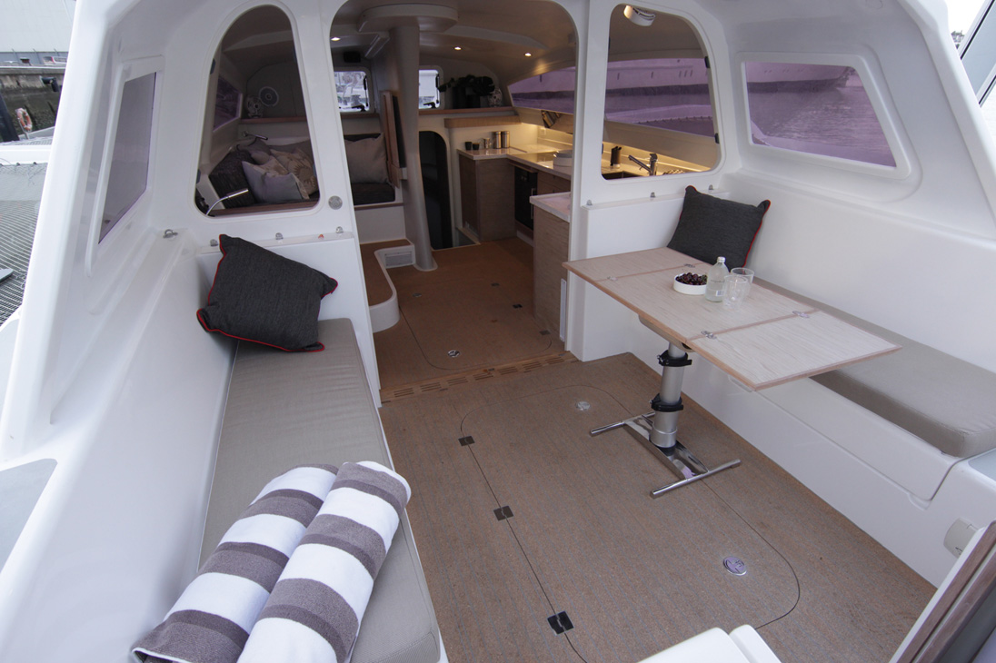 Le carré, le cockpit et la cuisine peuvent fusionner en un bel espace semi outdoor parfaitement protégé du vent, des embruns et du soleil (notez le carénage latéral qui ferme la zone pour les hautes vitesses). Ici, la porte de liaison est basculée et stockée sous le bimini, ainsi que les panneaux plexi adjacents rangés dans les alvéoles (juste en avant des coussins gris).